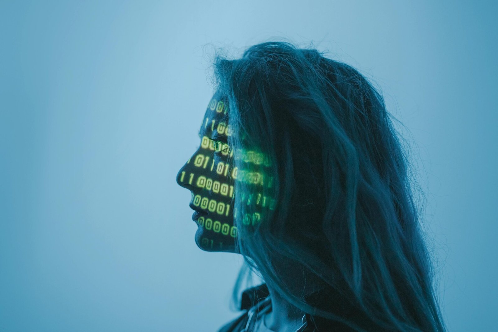 Zijaanzicht van een vrouw met binaire code geprojecteerd op haar gezicht, tegen een blauwe achtergrond.